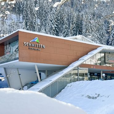 Das Bild zeigt das Bründl Sports Geschäft bei der Talstation der Schmittenbahn in Zell am See, umgeben von verschneiten Bäumen und winterlicher Landschaft. Das Gebäude ist modern und klar gestaltet.