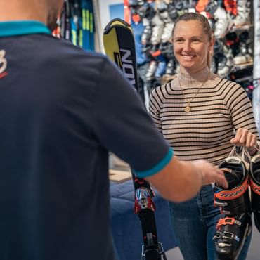 Eine Kundin übergibt dem Bründl Mitarbeiter gebrauchte Ski und Skischuhe