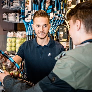 A customer gives his tennis racket to a staff member