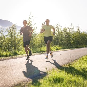 Two runners training together on a paved path in an alpine landscape