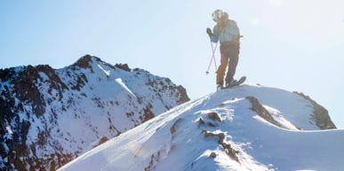 Ein Freerider steht auf einem Berg und blickt hinab ins Tal auf seine Abfahrt 