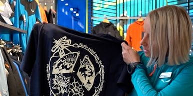 Bründl Sports employee stands in a shop and presents a T-shirt made from recycled Himalayan plastic bottles.