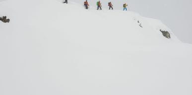 Eine Gruppe von Menschen besteigen den Berg im Winter um an einem Lawinenkurs teilzunehmen.
