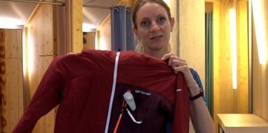 Bründl Sports Mitarbeiterin steht im Geschäft und stellt eine Ortovox Wanderjacke vor.