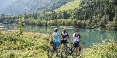 three cyclists are standing at the shore of a lake