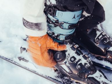 Header picture for Atomic Hawx Family magazine article. Skier buckling up ski boots.