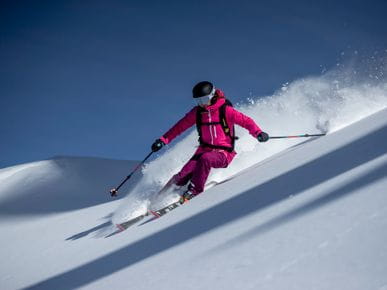 A woman dressed in a pink ski outfit making her turns in powder snow