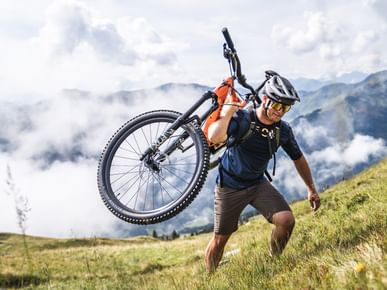 Der Mountainbiker trägt sein Fahrrad auf dem Rücken und klettert den Berg hinauf