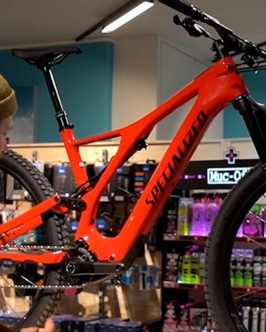 A Bründl Sports employee stands in a shop and presents a red Specialized bike.