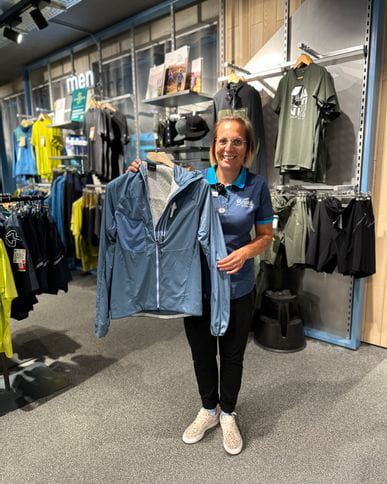 Bründl Sports Mitarbeiterin zeigt die neue PeakPerformance Jacke in blau.