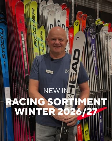A smiling Bründl Sports employee holds a HEAD ski in front of a wall displaying skis from various brands. The text reads “NEW IN – RACING SORTIMENT WINTER 2026/27”.