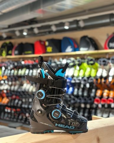 Head Kaliber Boa 2 ski boot displayed side-on in a modern ski shop, highlighting the Boa closure system with shelves of additional ski boots blurred in the background.