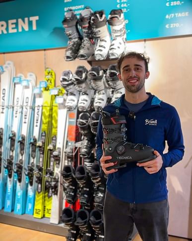 Ein Bründl Sports Mitarbeiter steht vor der Skiverleih Wand und hält einen Skischuh in der Hand. 