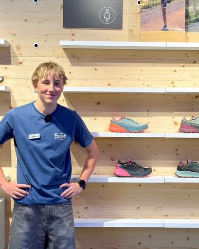 Bründl Sports Mitarbeiter vor einer Regalwand mit Schuhen aus dem Dynafit Trailrunning Sortiment