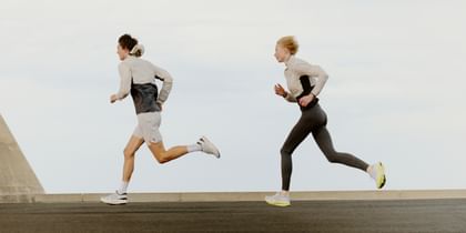 Two athletically dressed individuals are running dynamically side by side on a road under the open sky.