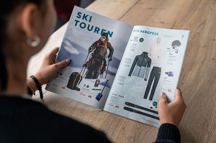 A person is flipping through the Magic Moments Magazine, showcasing various gear and clothing for ski touring