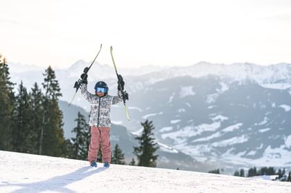 Glückliches Kind mit Skiern in der Hand am Berg bei Sonnenschein