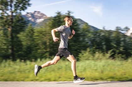 Runner runs in side view on a paved path through a green alpine landscape.