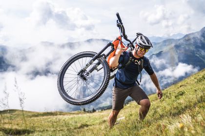 Der Mountainbiker trägt sein Fahrrad auf dem Rücken und klettert den Berg hinauf