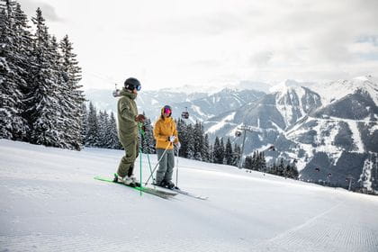 zwei Skifahrer unterhalten sich auf einer Skipiste, im Hintergrund die Schneelandschaft