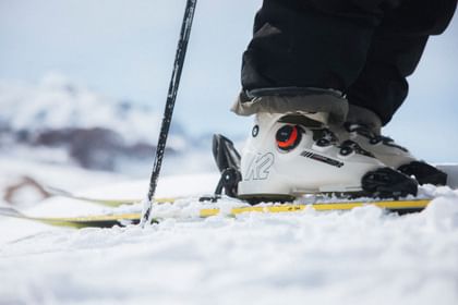 BOA Ski Boots K2 White BOA ski boot from K2, strapped into the binding on the ski on the slope. Snow-covered mountains in the background.