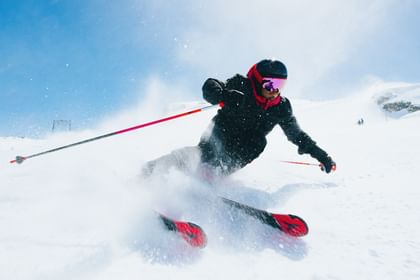 Atomic Redster Skier turning in the snow with Atomic Redster skis, snow spraying in the air, blue sky in the background.