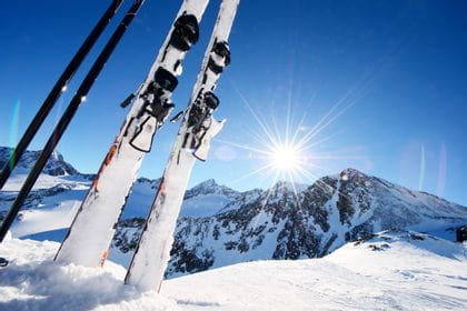 Skier in der Piste steckend, im Hintergrund Berge und die Sonne