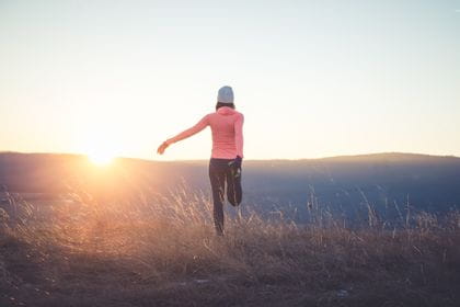 eine Läuferin dehnt sich, während im Hintergrund die Sonne aufgeht