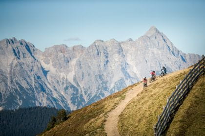 Downhill-bikers are climbing a mountain in the summery alps