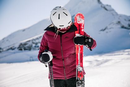 A female skier stands in the snow, her skis in one hand and her poles in the other hand