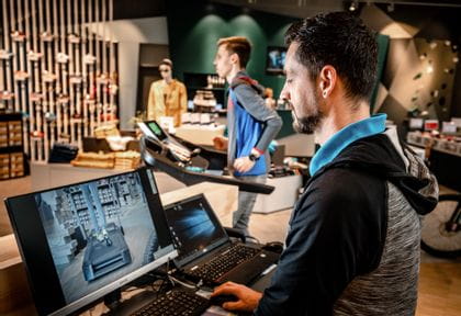 Der Mitarbeiter analysiert den Laufstil des Kunden am Computer, im Hintergrund läuft der Kunden am Laufband