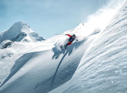 ein Skifahrer fährt im Tiefschnee bei blauem Himmel