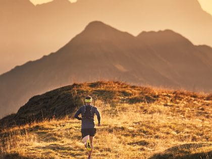 eine Person läuft in der Berglandschaft, im Hintergrund die entfernten Berge gefärbt in unterschiedlichen Orange-tönen