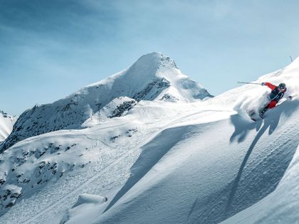 ein Skifahrer fährt im Tiefschnee bei blauem Himmel