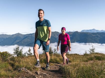 Eine Frau und Herr in Martini Outfit beim Wandern. Im Hintergrund die Berge. 