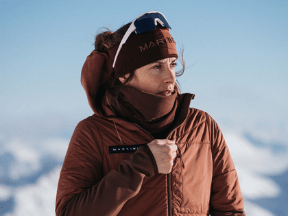 Woman wearing a warm Martini insulated jacket looking into a winter alpine landscape under a clear sky.