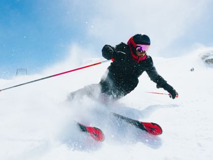 Skier turning in the snow with Atomic Redster skis, snow spraying in the air, blue sky in the background.