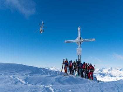 Gruppenbild auf einem Gipfel beim Heliskiing im Hintergrund ein Helikopter.