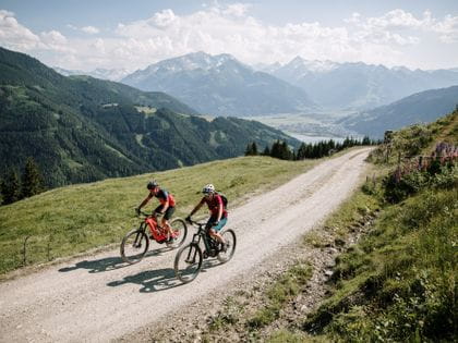 Two cyclists ride up the mountain on a gravel road.<br/>