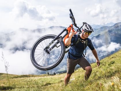 Der Mountainbiker trägt sein Fahrrad auf dem Rücken und klettert den Berg hinauf