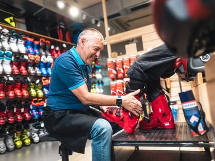 Bootfitting A Bründl Sports employee assists a customer in fitting ski boots. The employee sits in front of a wall of colorful ski boots, ensuring the perfect fit on the customer's foot.