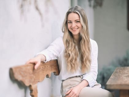 Paula lächelt in die Kamera, auf einer Holzbank sitzend
