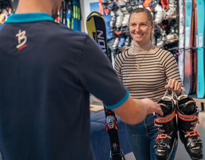 Eine Kundin übergibt dem Bründl Mitarbeiter gebrauchte Ski und Skischuhe