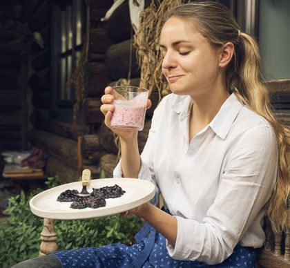Paula mit einem Teller Moosbeernocken und einem Glas Preiselbeerbuttermilch in der Hand