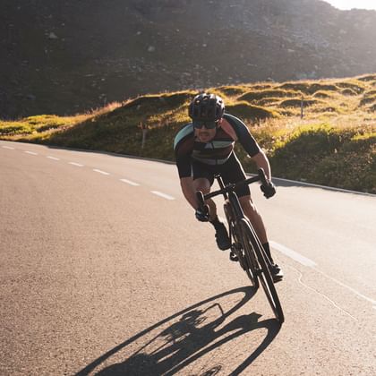 A racing cyclist dressed in Löffler bike clothing rides downhill on a road. 