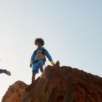 A female hiker and a male hiker jump over rocks in the evening sun