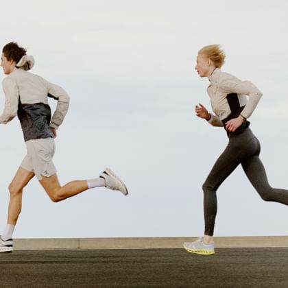 Two athletically dressed individuals are running dynamically side by side on a road under the open sky.