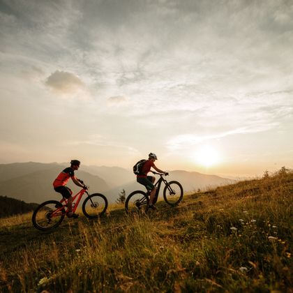 zwei Fahrradfahrer fahren im Sonnenuntergang einen Berg hinauf
