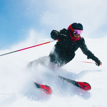 Skier turning in the snow with Atomic Redster skis, snow spraying in the air, blue sky in the background.