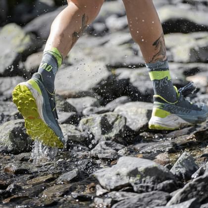 Dynafit trail running shoes running through a mountain stream on a technical alpine trail.